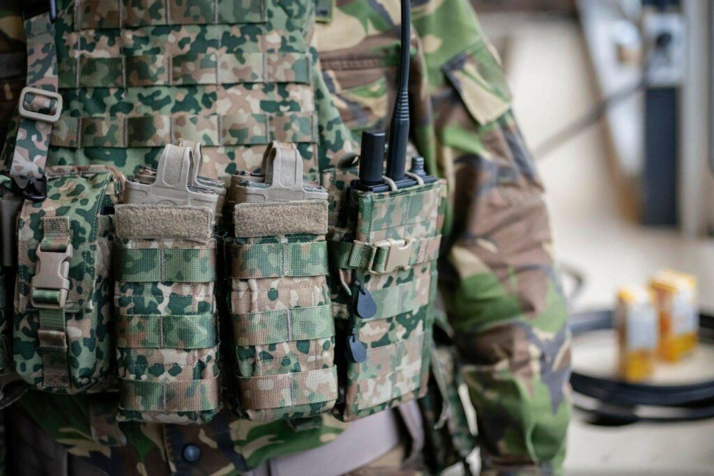 Close-up view of military radio pouches and equipment attachments on a camouflage tactical vest.