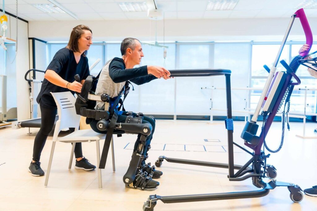 A physiotherapy assistant lifts a disabled person with a robotic skeleton.