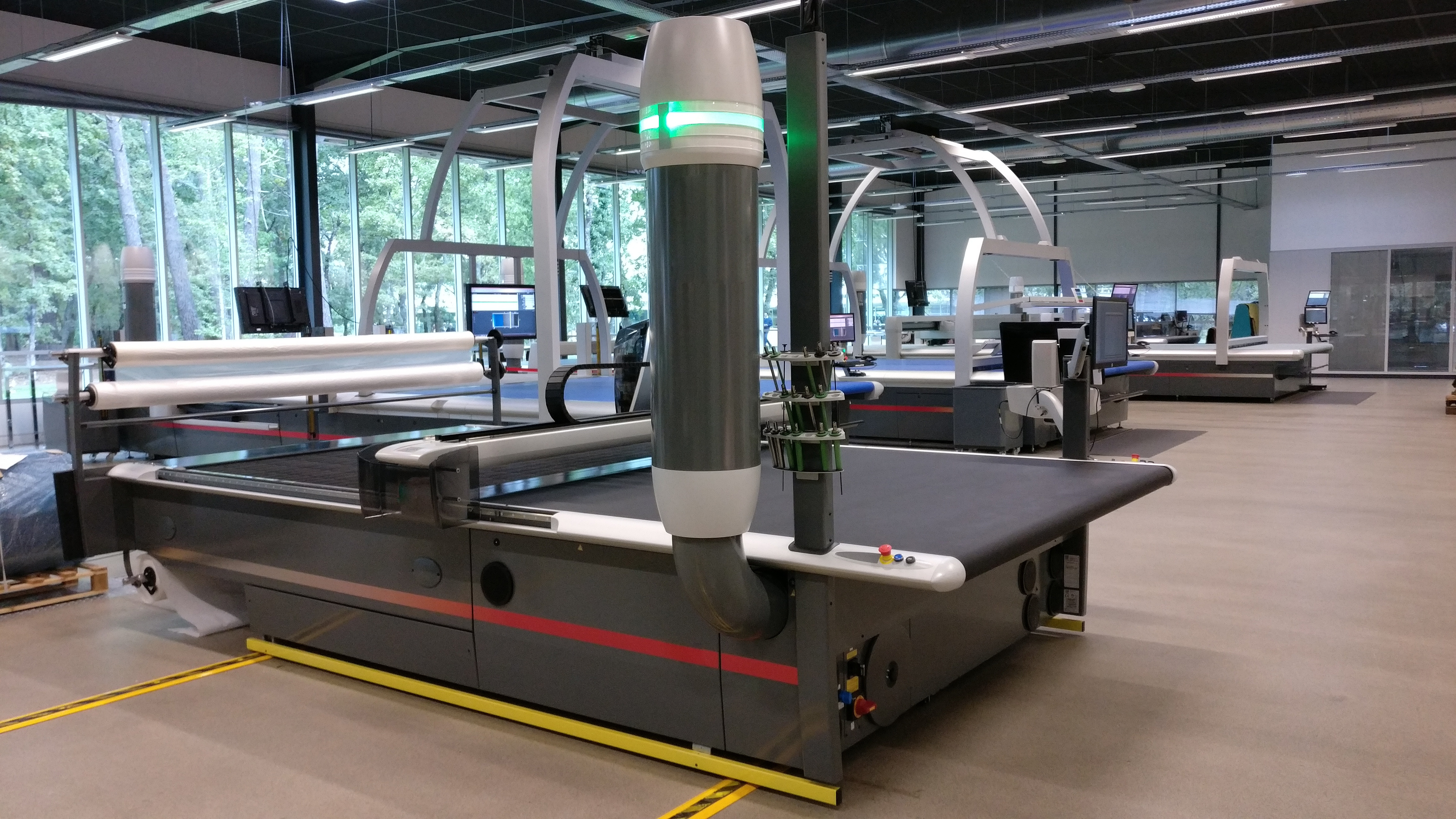  A large industrial CNC cutting machine is operating on a dark blue textile material in a modern, well-lit factory setting.